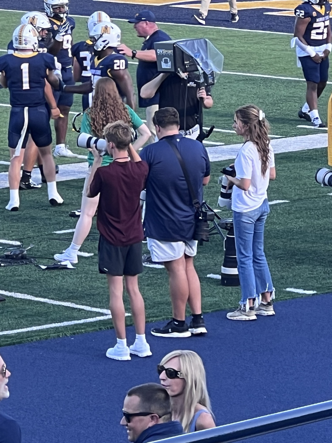 Luke in a burgundy shirt photographing the action from the Murray State sideline